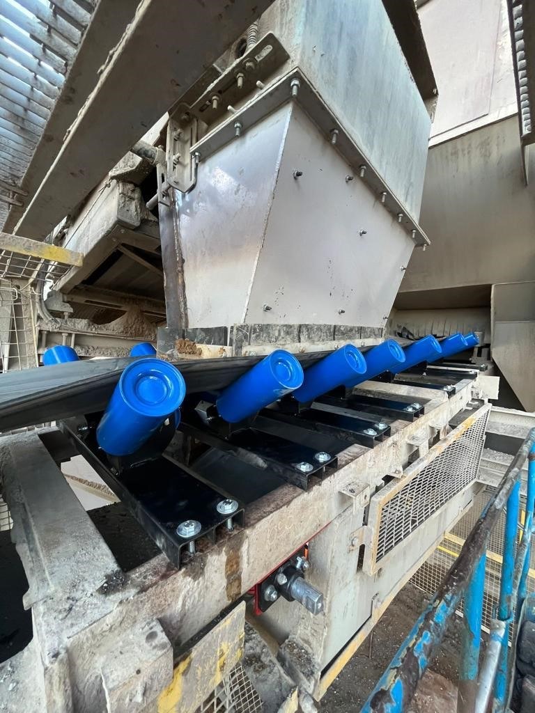 Lined transfer chute above troughing rollers on a conveyor